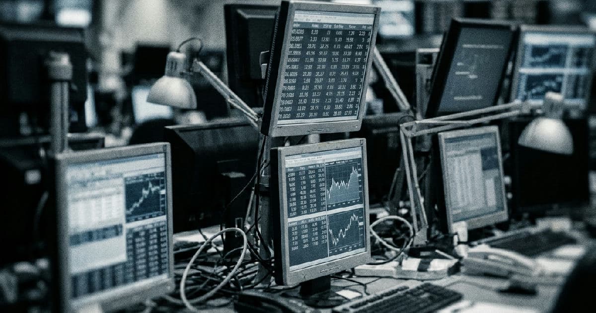 Multiple monitors display financial market data and trading charts in muted tones.